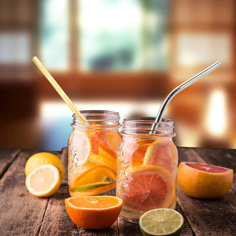 Deux bocaux remplis de boissons aux agrumes avec une paille dorée et une paille argentée, citron et pamplemousse en premier plan.