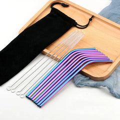 Pailles cocktail multicolores irisées courbées disposées sur un plateau en bois avec pochette et brosses de nettoyage.