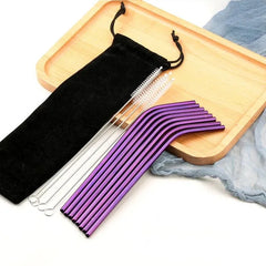 Pailles cocktail violettes courbées disposées sur un plateau en bois avec pochette noire et brosses de nettoyage.