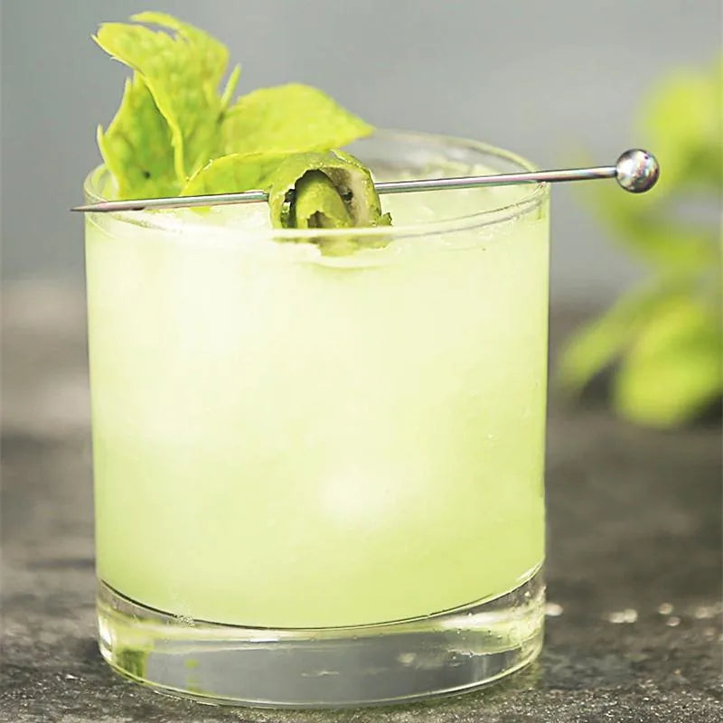 Pic à cocktail argenté garni de feuilles de menthe fraîche posé sur un verre de mojito glacé.