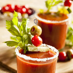 Bloody Mary garni d'une olive, d'une cerise et de céleri sur un pique argenté, avec bord du verre givré de sel.