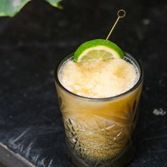 Verre à cocktail avec zeste d'agrume et pique doré, présenté dans une ambiance de bar sombre et chaleureuse.