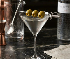 Pic à cocktail épée piquant trois olives vertes dans un martini au bar.