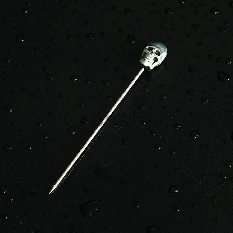 Gros plan du pic à cocktail tête de mort posé sur une surface noire parsemée de gouttes d'eau.