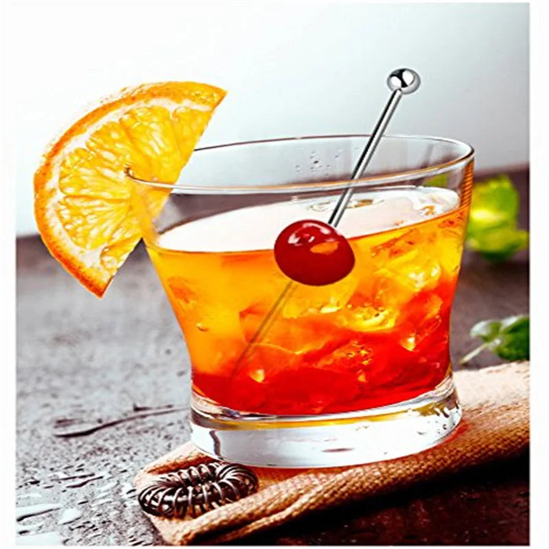 Pic à cocktail irisé plantant une cerise dans un cocktail Old Fashioned garni d'une tranche d'orange.