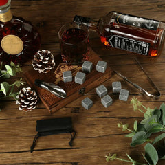 Coffret pierre à whisky en ambiance nature avec bouteilles de whisky, pommes de pin et feuillage