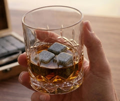 Main tenant un verre de whisky avec trois pierres à whisky en granit