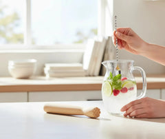 Le pilon en bois posé sur un plan de travail à côté d'une carafe de mojito glacé au citron vert et framboises.