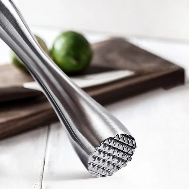 Gros plan macro sur l'embout godronné en inox du pilon, avec un citron vert flou en arrière-plan.