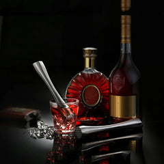 Le pilon en inox posé devant des bouteilles de cognac et un verre ambré sur fond noir, dans une ambiance bar chic.