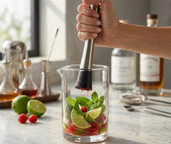 Pilon à cocktail écrasant de la menthe, du citron vert et des framboises dans un verre à mélange.