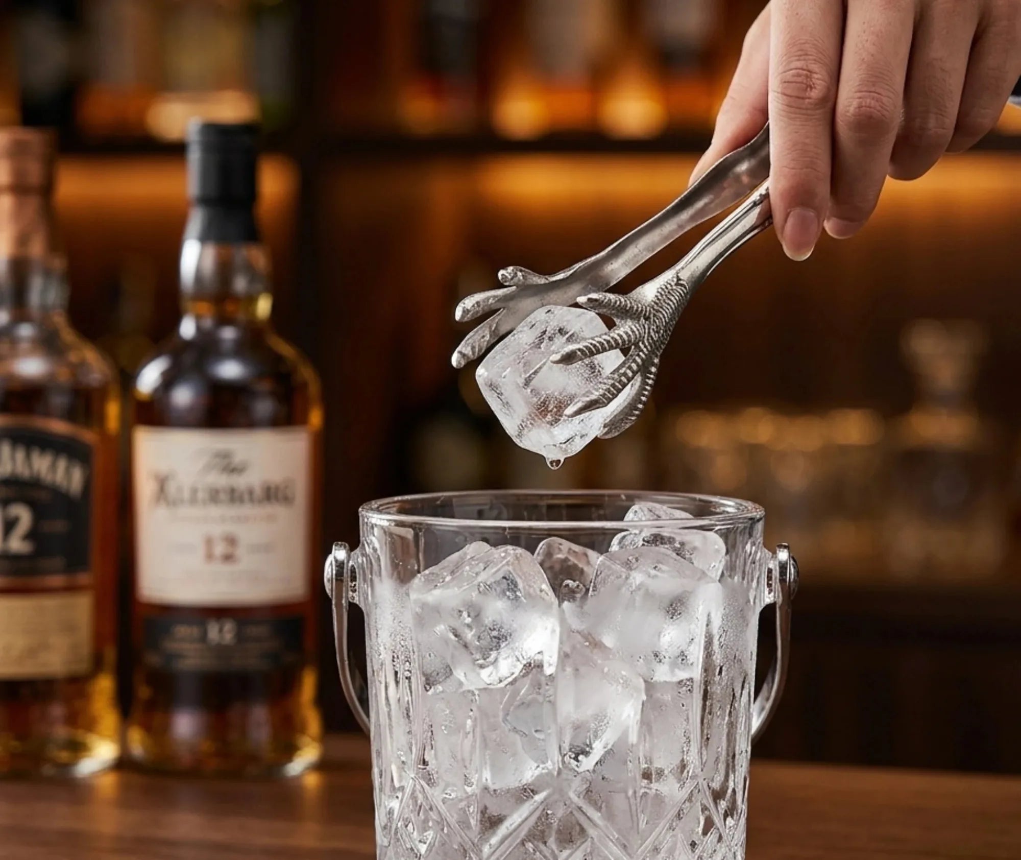 Pince à glaçons serres d'aigle servant un glaçon au-dessus d'un seau, bouteilles de whisky en arrière-plan de bar