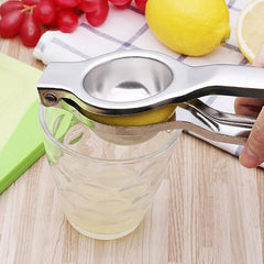 Presse-citron manuel utilisé pour remplir un verre de jus de citron frais sur une planche en bois, avec des raisins et un citron à proximité.
