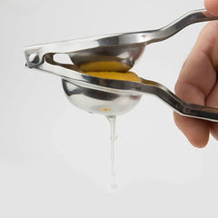 Main pressant une moitié de citron dans le presse-citron manuel, avec une goutte de jus qui s'écoule sur fond blanc.