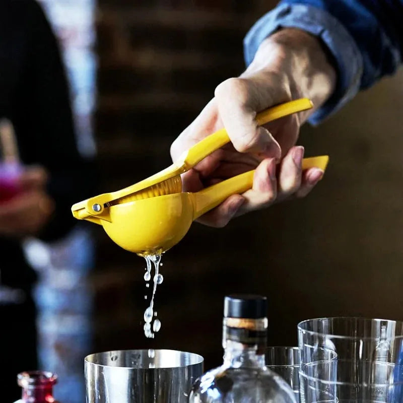 Main d'un barman pressant un citron avec le presse-agrumes jaune au-dessus de verres à cocktail, ambiance bar sombre.