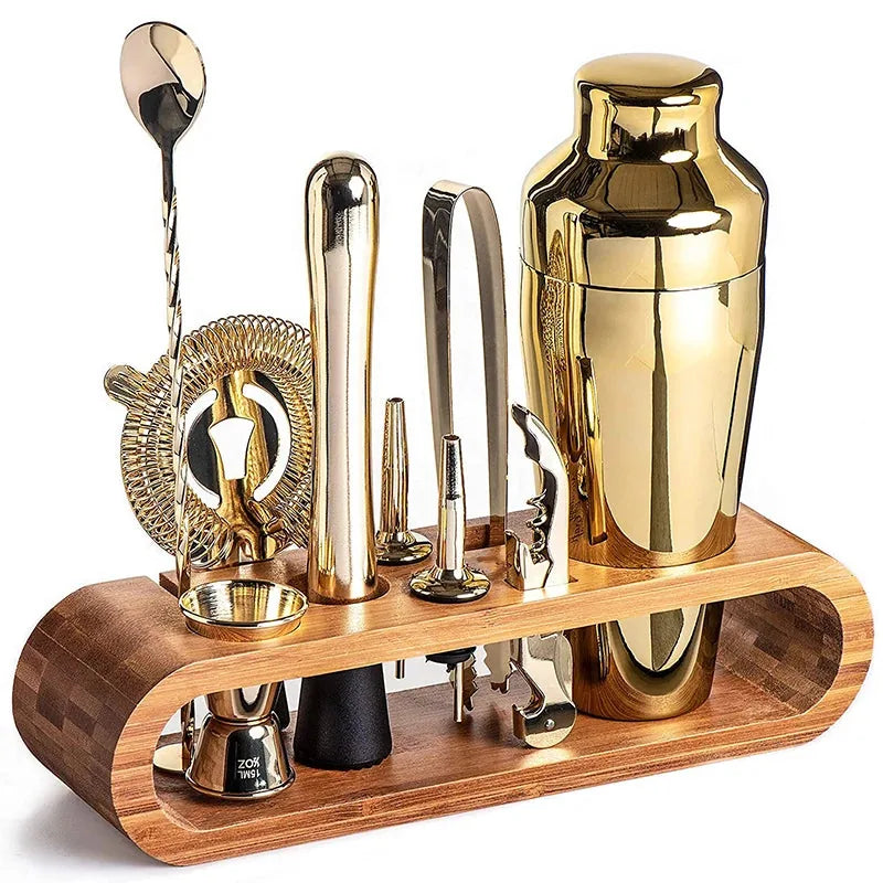 Set cocktail en bois avec accessoires dorés (shaker, doseur, cuillère à mélange, pince à glaçons, tire-bouchon) présentés debout sur leur support en bambou, photo sur fond blanc