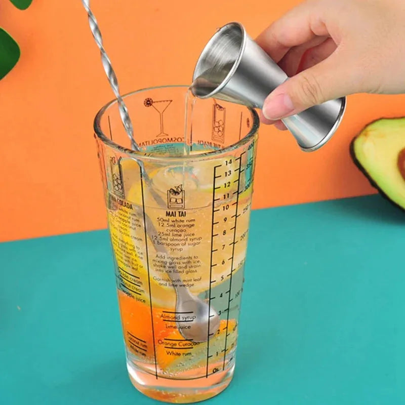 Une main verse le doseur dans le verre mesureur gradué du set barman cocktail, avec recettes de cocktails imprimées et avocat en arrière-plan