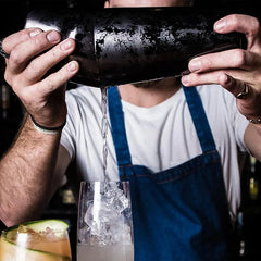 Un barman verse un cocktail glacé depuis le Shaker Boston Noir lors de sa préparation.