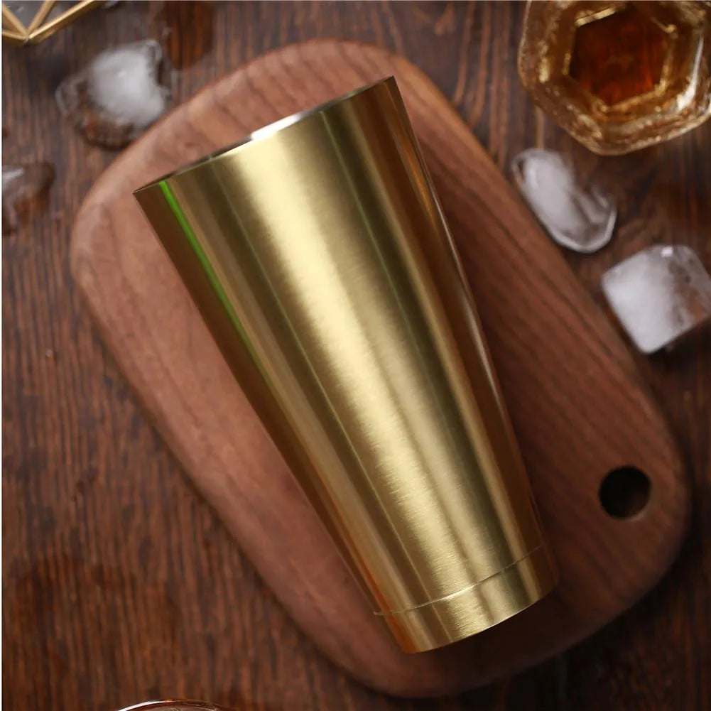 Gros plan du gobelet métallique doré du shaker Boston posé sur une planche en bois avec glaçons et verre de whisky