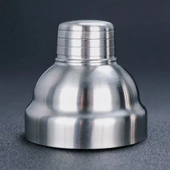 Gros plan sur le bouchon doseur strié du shaker cocktail classique en inox, posé seul sur fond sombre.