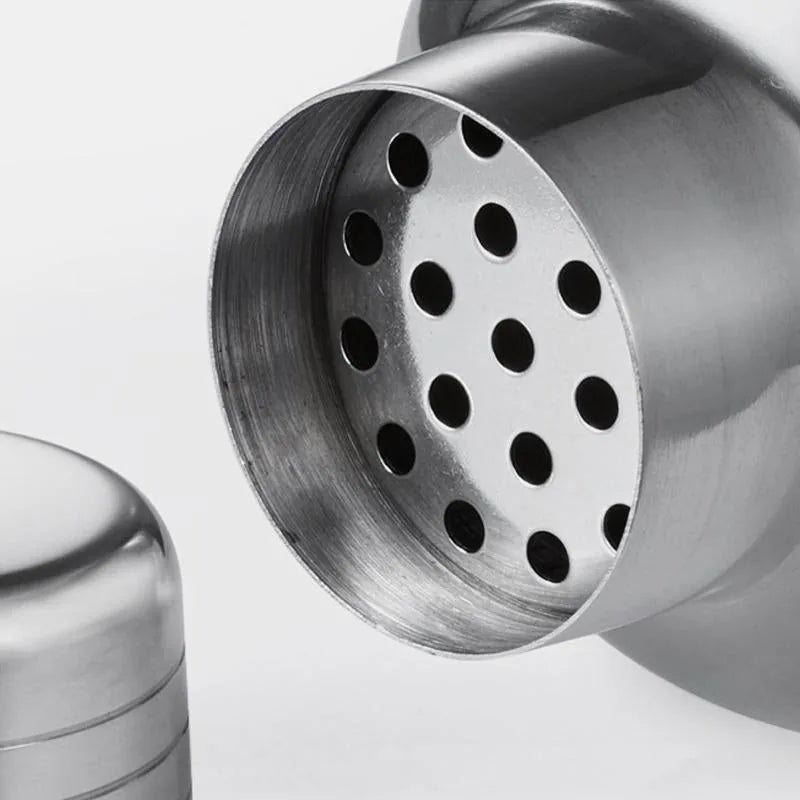 Gros plan sur la passoire perforée en inox du shaker cocktail classique, avec le bouchon doseur posé à côté.