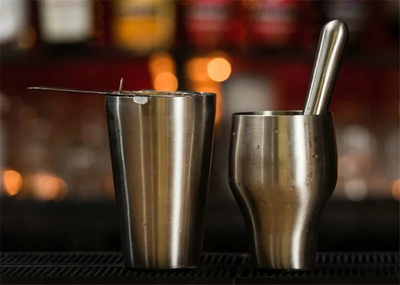 Deux pièces du shaker à cocktail argenté posées sur un comptoir de bar, avec bouteilles floutées en arrière-plan