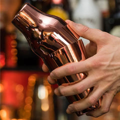 Barman tenant le shaker cocktail cuivré en train de préparer une boisson dans un bar