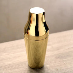 Shaker cocktail doré posé sur une table en bois dans une mise en situation d'intérieur