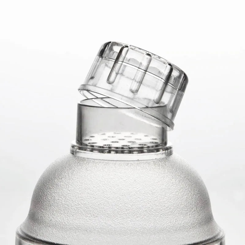 Détail du bouchon verseur transparent strié soulevé au-dessus de la grille filtrante du shaker à cocktail gradué.
