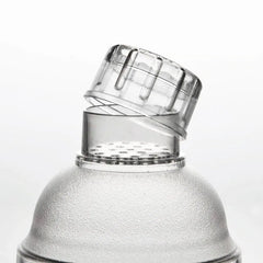 Détail du bouchon verseur transparent strié soulevé au-dessus de la grille filtrante du shaker à cocktail gradué.