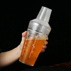 Une main tient le shaker à cocktail en plastique rempli d'un cocktail orange sur fond noir, mettant en valeur sa taille.