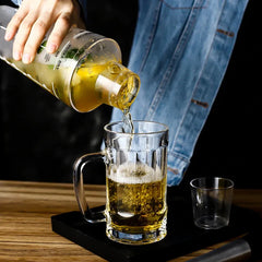 Le shaker en plastique verse un cocktail doré dans une chope en verre posée sur un plateau noir.