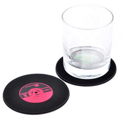 Sous-verre disque vinyle noir avec étiquette rose associé à un verre à whisky en cristal, sur fond blanc.