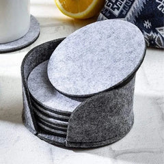 Pile de sous-verres en feutrine grise avec un sous-verre incliné au premier plan, à côté d'un demi-citron sur un plan de travail en marbre.