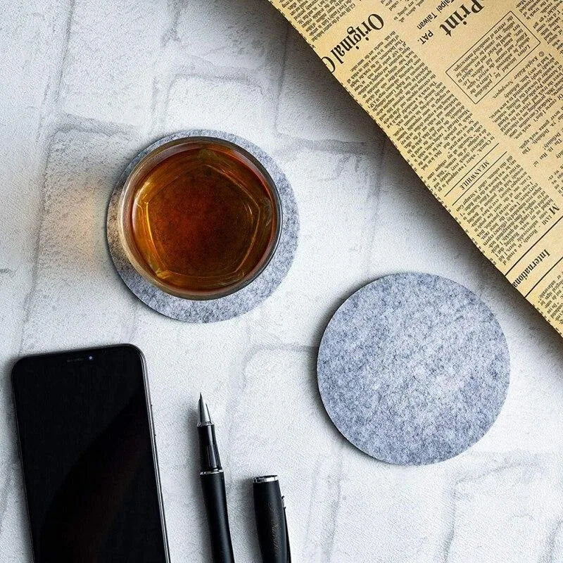 Verre de whisky posé sur un sous-verre en feutrine grise, entouré d'un journal, d'un smartphone et d'un stylo sur une table en marbre.