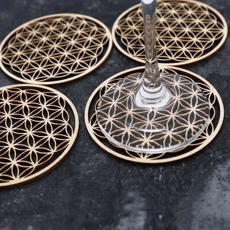 Gros plan sur plusieurs sous-verres Fleur de Vie en bois disposés sur un fond gris ardoise, avec le pied d'un verre posé sur l'un d'eux.