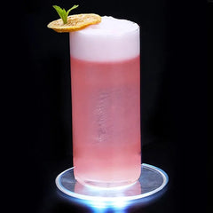 Cocktail rose mousseux garni de menthe fraîche et d'une rondelle d'agrume séché, servi sur le sous-verre lumineux.