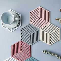 Vue aérienne d'un assortiment de sous-verres hexagonaux colorés disposés en cercle autour d'un sous-verre métallique doré avec une tasse de thé.