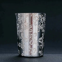 Verre à mélange en acier inoxydable au motif floral gravé, photographié en packshot élégant sur fond noir.