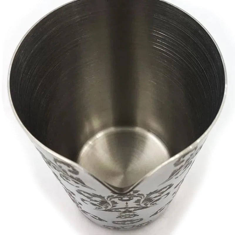 Vue plongeante sur l'intérieur du verre à mélange en acier inoxydable, laissant apparaître le bec verseur et le motif floral gravé.