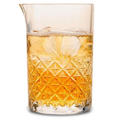 Verre à mélange en cristal facetté rempli de glaçons et d'une boisson ambrée, photographié sur fond blanc