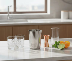 Kit de mixologie complet avec verre à mélange en inox, verres à cocktail, jigger en cuivre et fruits frais sur un plan de travail de cuisine