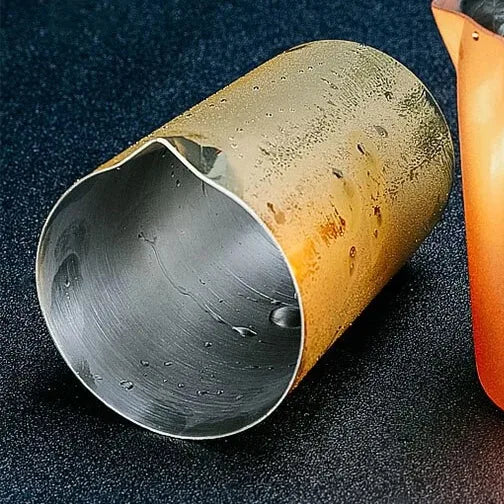 Gros plan sur le bec verseur et l'intérieur poli du verre à mélange doré, avec des gouttes d'eau visibles.