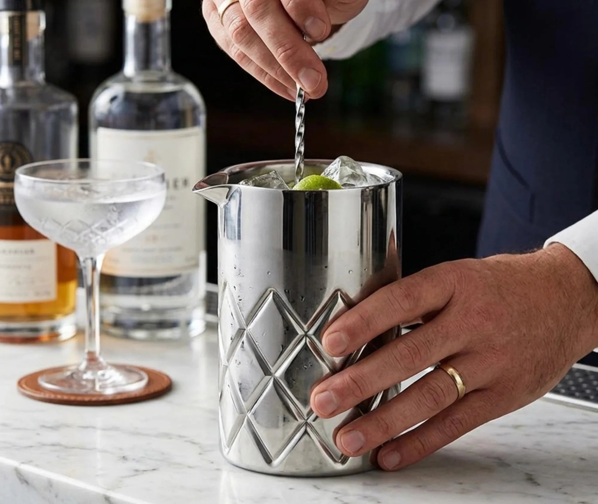 Barman préparant un cocktail en remuant glaçons et rondelle de citron vert dans le verre à mélange en inox