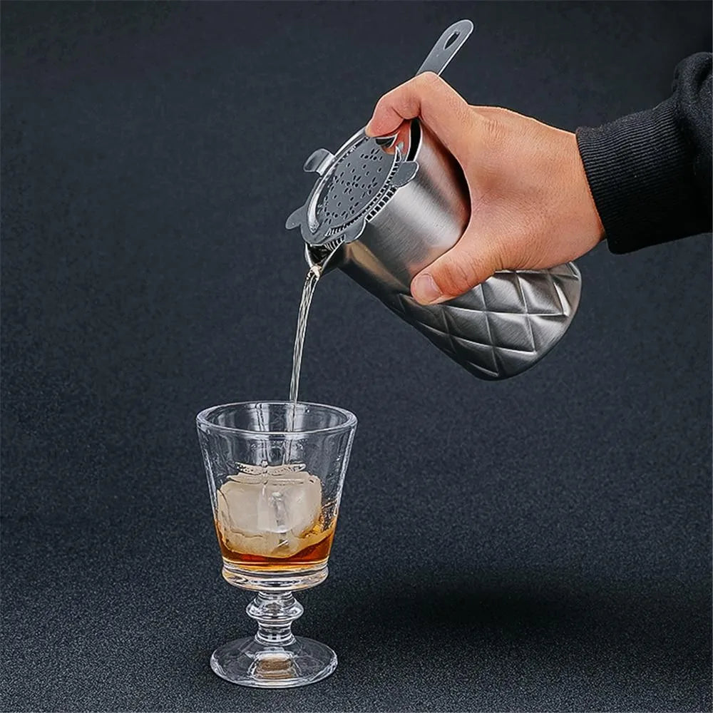 Main versant un cocktail ambré à travers la passoire du verre à mélange en inox dans un verre à glaçons