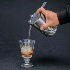 Main versant un cocktail ambré à travers la passoire du verre à mélange en inox dans un verre à glaçons