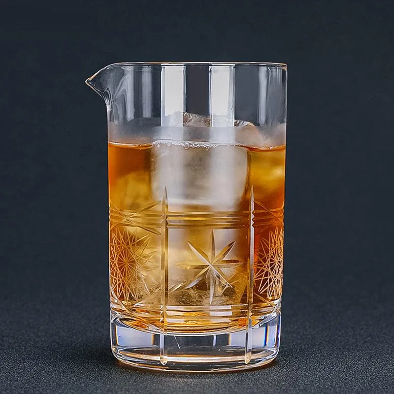 Verre à mélange vintage à motifs étoilés gravés, rempli de cocktail ambré et de glaçons, mis en valeur sur fond noir.