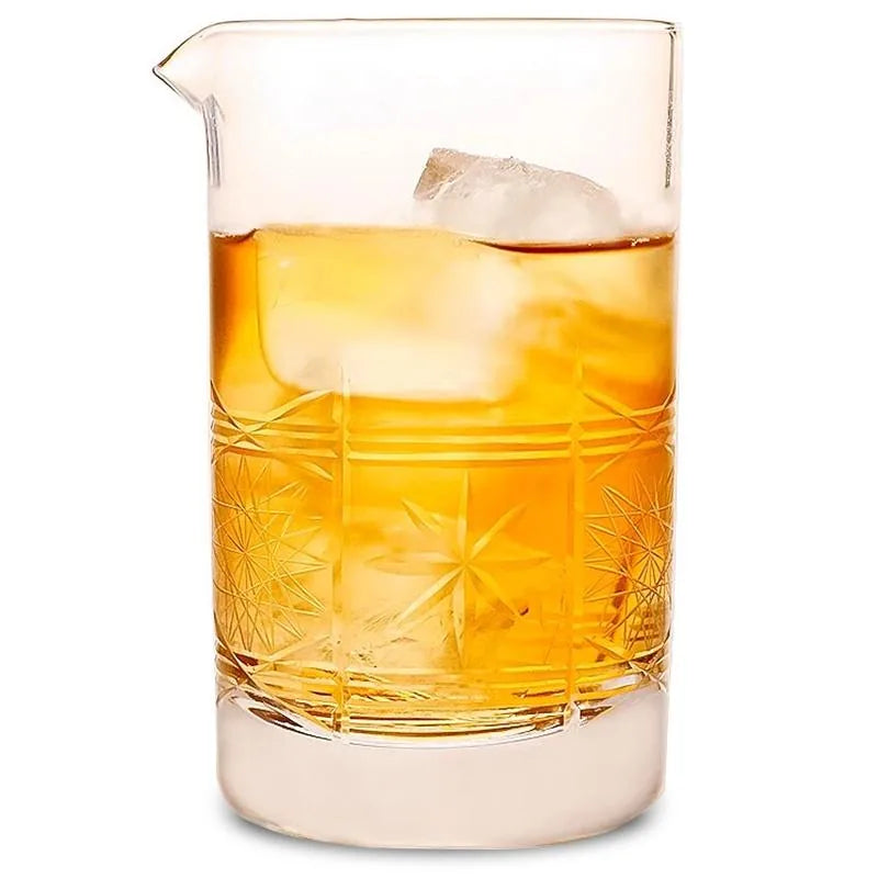 Verre à mélange vintage en cristal taillé rempli de whisky ambré et d'un gros glaçon, photographié sur fond blanc.