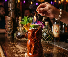 Cocktail tiki flambé servi dans le verre à rhum Tiki, décoré de menthe, ananas et citron vert, dans une ambiance de bar tropical