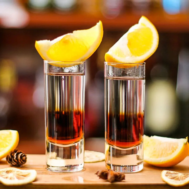 Deux verres à shot longs avec un cocktail dégradé ambré et rouge, garnis de citron